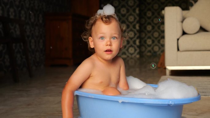 可爱的小男孩坐在婴儿浴盆里，眼神直视，微笑，慢镜头