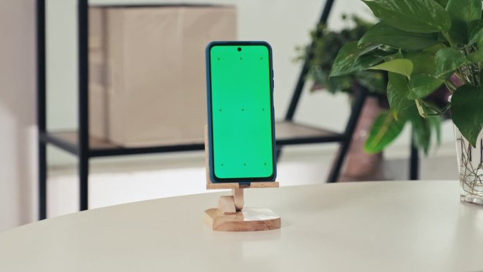 绿色色度键屏的智能手机在客厅桌子上的木制支架上