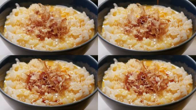 鸡蛋煮米饭，上面放着鲣鱼片。放酱油的视频。特写镜头。