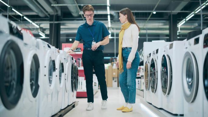 顾客在选择洗衣机时与零售电子商店顾问对话。寻找洗衣用具的女性。顾客在现代零售商店里探索产品