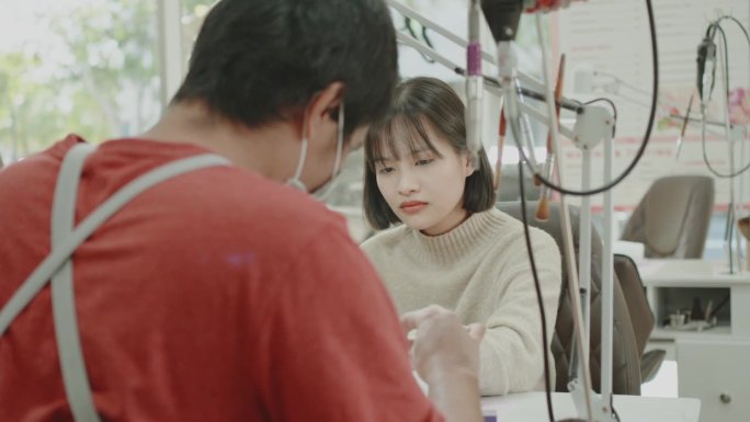 年轻的亚洲妇女在美甲沙龙接受男美容技师的美甲