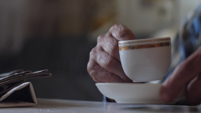退休老人看完报纸，用杯子喝着美味的早茶。老人的居家休闲。一个老人端着一杯咖啡的手