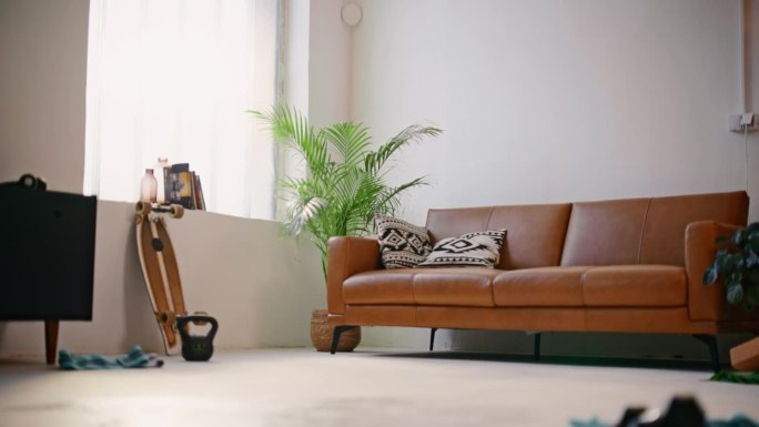 在现代客厅里，棕色皮沙发旁边的地板上放着滑板和壶铃。简约，居家生活，积极的生活方式，室内设计。以8K