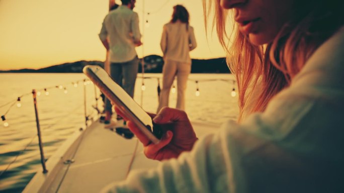 一个女人坐在船上玩手机。朋友们在甲板上消磨时光