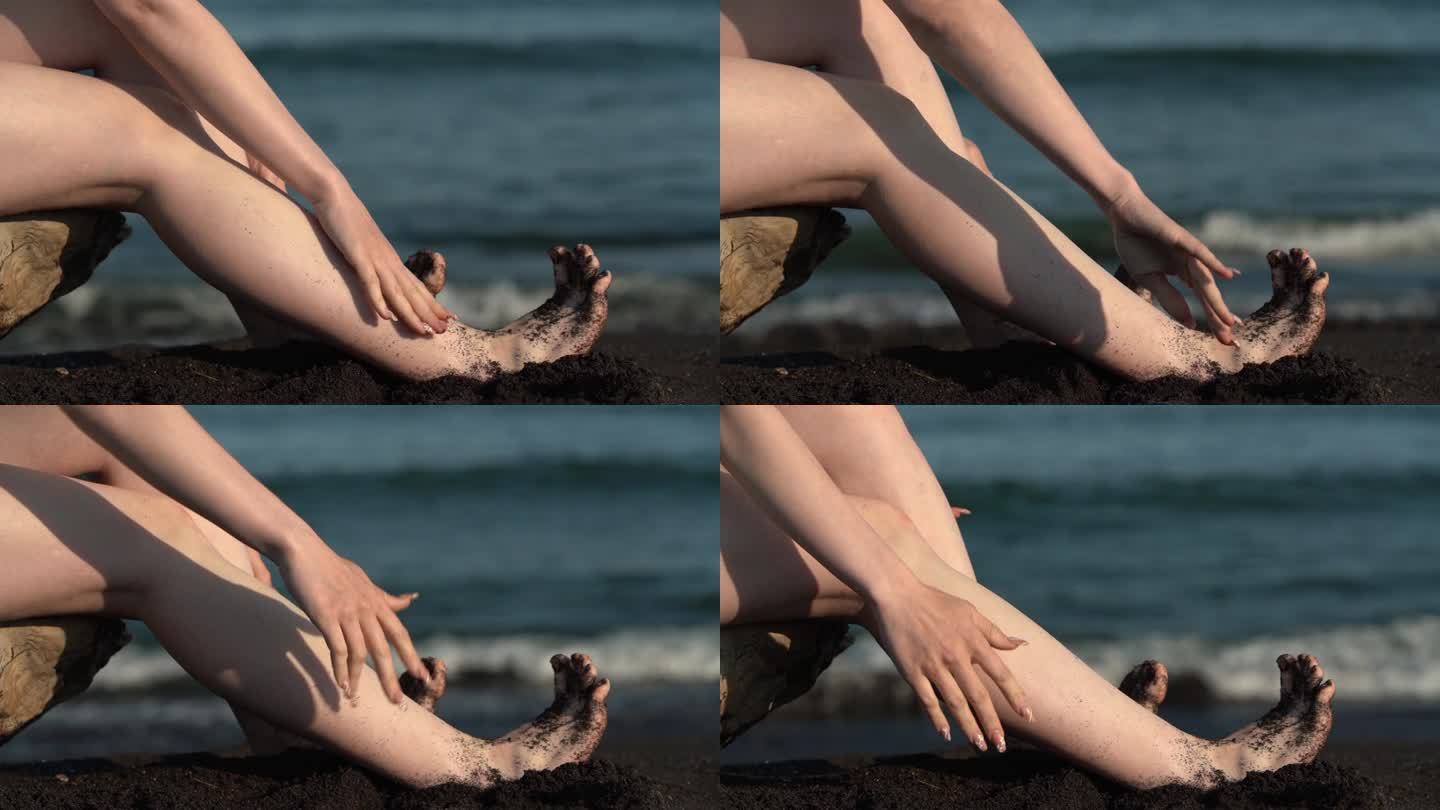 在海浪的背景下，赤脚女人在沙滩上把脚从黑沙滩上抖下来的特写