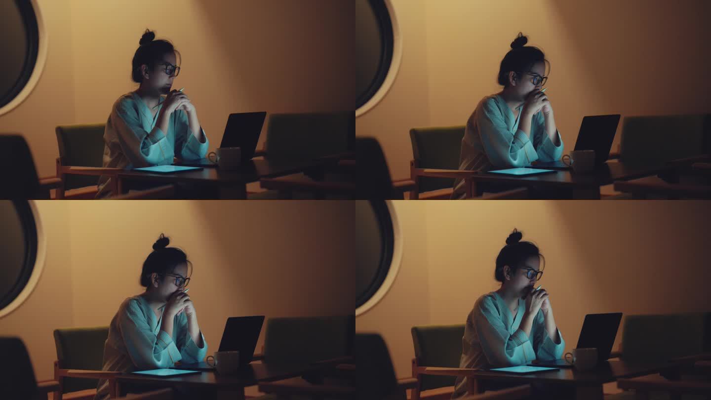 劳累过度的亚洲女性自由撰稿人，晚上在客厅用平板电脑和笔记本电脑加班。
