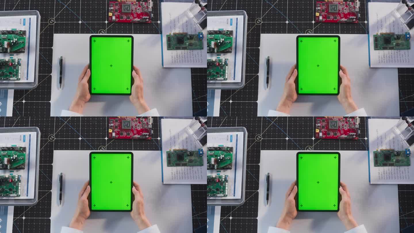 一个匿名的工程师手持平板电脑与模拟绿屏Chromakey显示器垂直俯视视图。工业专家观看电子产品开发