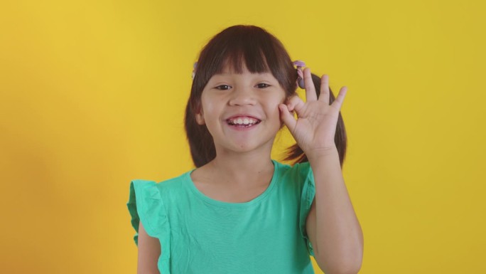 可爱的女孩在黄色的工作室背景下用手指做ok的手势。