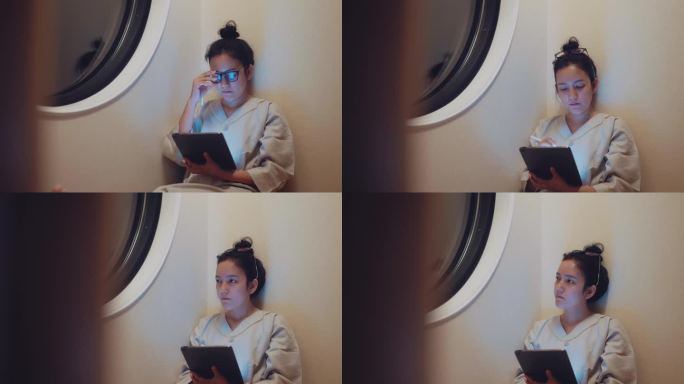 亚洲女性是内容创造者，坐在沙发上用她的数码平板电脑创作和享受夜晚。