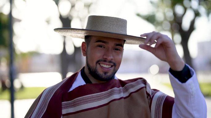 头部肖像，微笑的拉丁美洲年轻人穿着智利华索服装，拿着帽子在街上