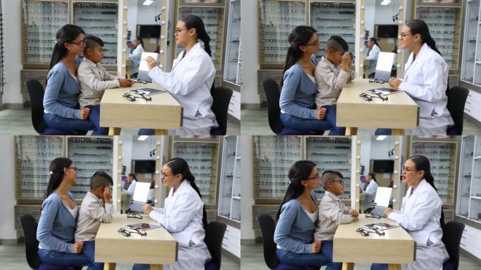 拉丁美洲男孩坐在妈妈的腿上在眼镜店试眼镜