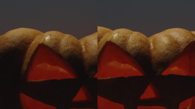 垂直视频。一个万圣节南瓜站在沙滩上，背景是夕阳，从上面照下来。特写镜头。