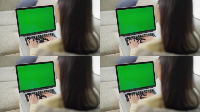 一个身份不明的女人沉浸在办公室工作的肩膀上，在沙发上舒适的家庭工作空间里使用一台带有绿屏模拟显示的笔