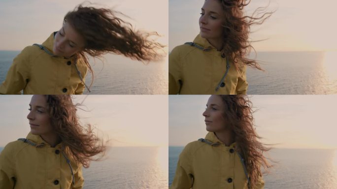 年轻女子的特写肖像与红头发吹在风中看着日落在海洋女孩穿着黄色雨衣徒步旅行在苏格兰慢动作