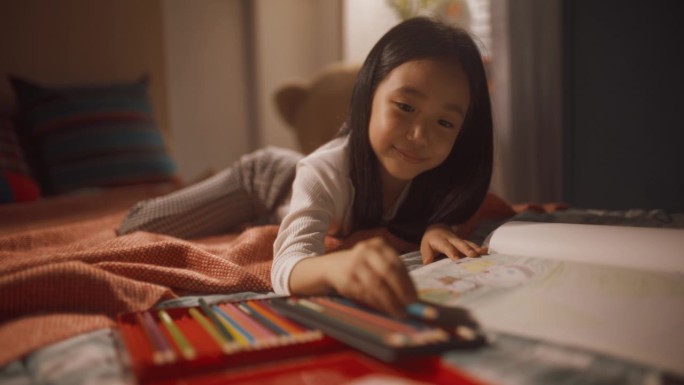 可爱的韩国小女孩用彩色铅笔给孩子画全家福。小孩子躺在床上，用不同的铅笔为她的父母做一件艺术品