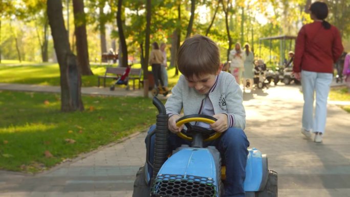 一个快乐微笑的小男孩开着玩具拖拉机在公园里玩耍。孩子们在公园里玩耍，种地，开车。
