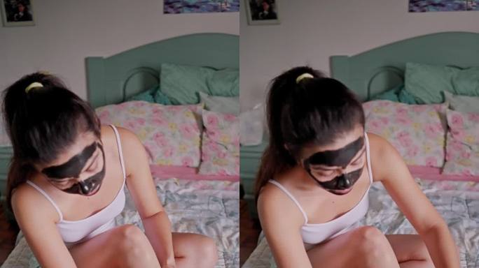 美容护理:西班牙年轻女子用木炭面膜，用蜡纸去除腿上的毛发，坐在床上。