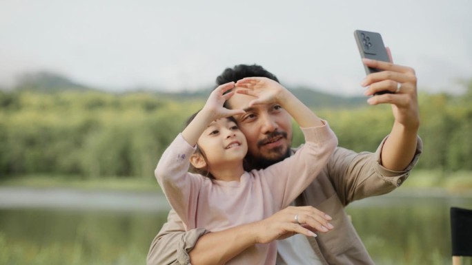 度假时在草地上露营，一对快乐的父亲和女儿微笑着坐在相机前拍照。