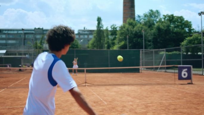 在红土场上，两名年轻的网球运动员正在为冠军而训练，他们正在集中精力进行比赛，用球拍使劲击球