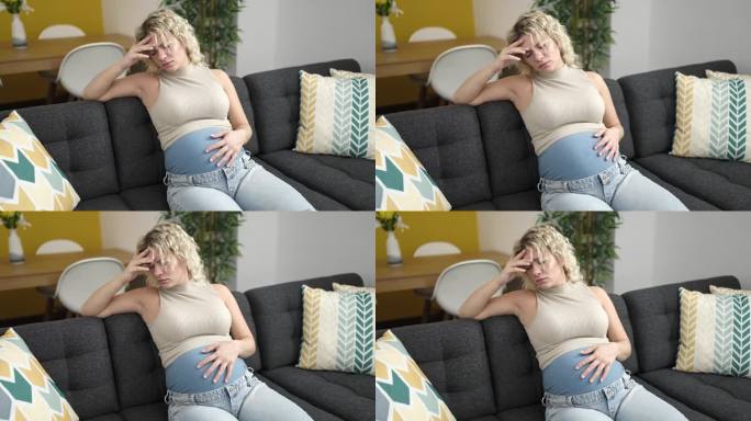 年轻的孕妇坐在家里的沙发上，神情紧张地摸着肚子