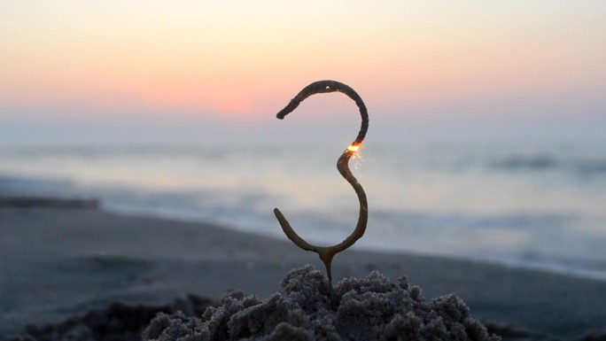 孟加拉火火花在数字3的形状燃烧和闪闪发光在沙滩上的海岸在日落的黎明。概念假期生日新年聚会庆祝