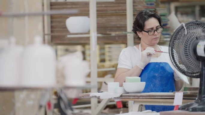 陶瓷厂的工人正在用刷子擦拭上了釉的盘子