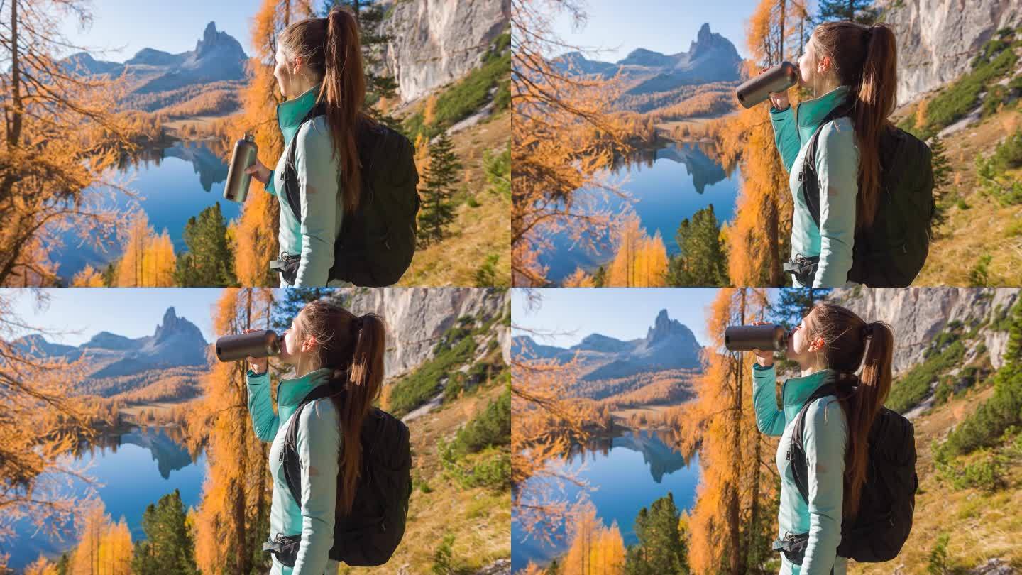 女徒步者休息，喝水，欣赏美丽的秋山景观