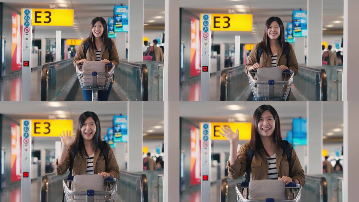 亚洲女乘客推着机场行李车，走在机场的自动扶梯上，微笑着向镜头挥手，慢动作镜头