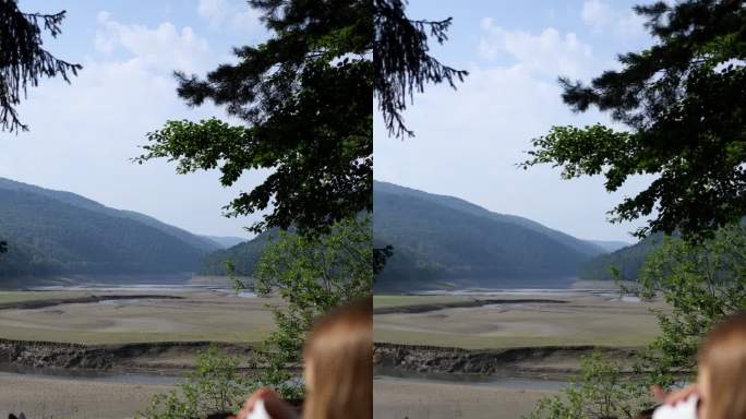 一个穿着夏装的女孩躺在山中的自然躺椅上，喝着白色马克杯里的咖啡，背景是一个干涸的湖水。垂直视频