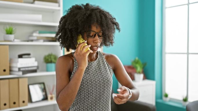 非洲裔美国女商人愤怒地在办公室用智能手机打电话，看手表