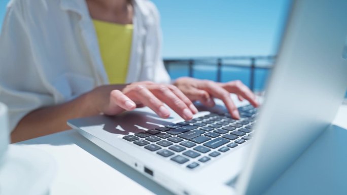 在美丽的海景露台上，女人在笔记本电脑键盘上打字。近距离看女人的手在电脑上写字。旅游，自由职业者，项目