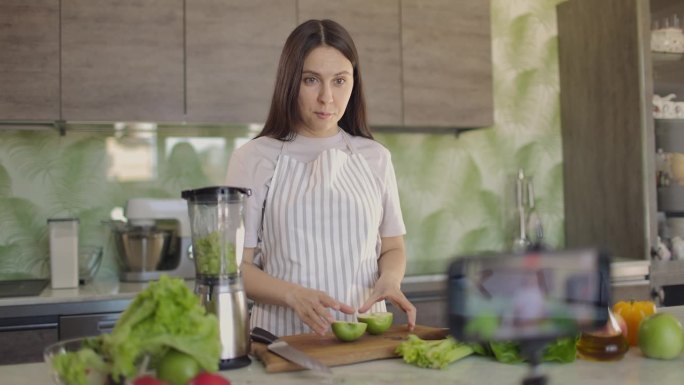 快乐的博主女孩谈论健康的生活方式和拍摄视频食谱。女孩对着智能手机摄像头看了看并说话。慢动作