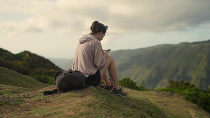 坐在世界之巅的女人。看着山下山谷的景色，发短信