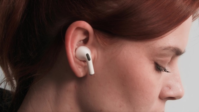 现代科技，年轻女子将无线耳机插入耳朵听音乐，特写