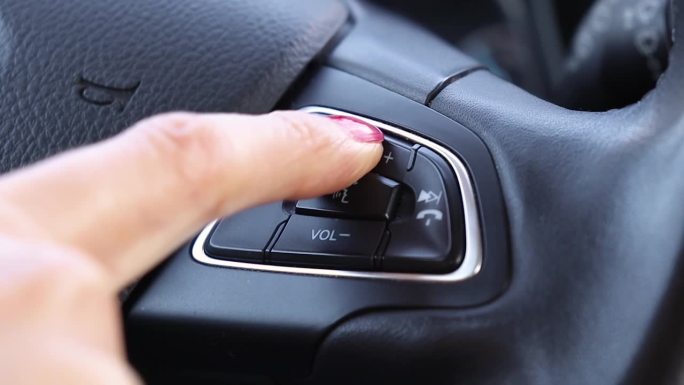 驾驶员按下汽车方向盘上的车载收音机音量按钮