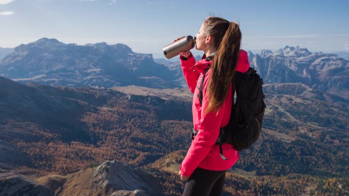 女人用可重复使用的瓶子补水，同时俯瞰山谷，背景是山脉