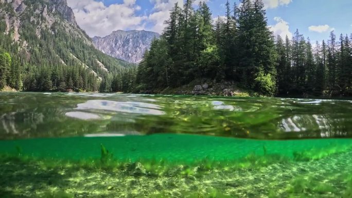 半水下拍摄的高山湖泊与清澈的水在奥地利的阿尔卑斯山。相机潜入湖泊，岩石山脉和森林的背景。高山自然，格
