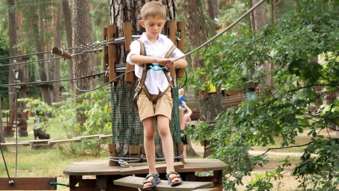 夏令营中，一个小男孩从悬挂在两棵树之间的摇摇欲坠的吊桥上走过。儿童运动，暑假，户外娱乐，童子军