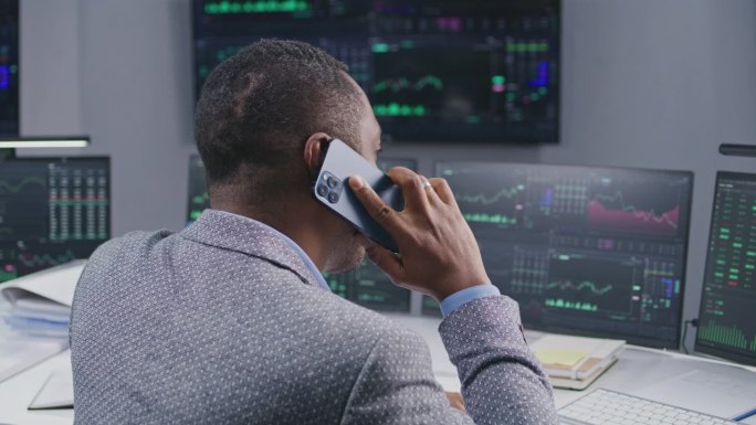 非裔美国男性股票交易员通过电话交谈，在经纪人办公室工作