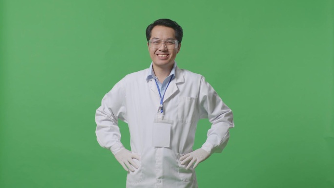 亚洲男性科学家两手叉腰站在实验室的绿幕背景上，微笑着看着镜头
