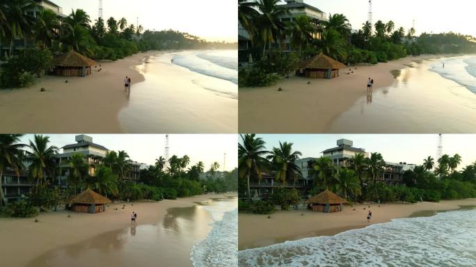 一对夫妇手牵着手走在热带海滩上，在日出时沿着海洋的潮汐漫步。男友和女友在海边沙滩上靠近水，拥抱，亲吻