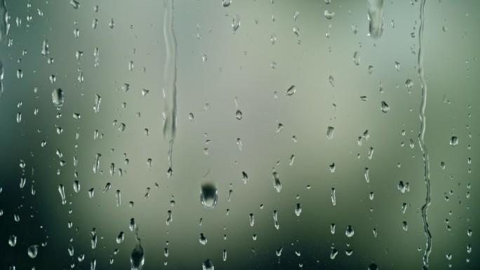 雨滴在绿色的背景下滑下窗户