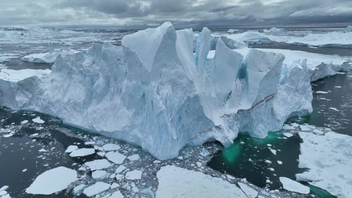 在格陵兰岛伊卢利萨特附近的巨大冰山附近飞行。冰山碎块掉入水中。空中北极自然景观，全球变暖和气候变化的