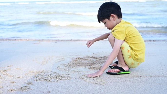 亚洲可爱的男孩正在沙滩上玩沙子和写字，慢动作的场景