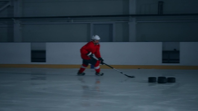 一名身穿红色运动衫的熟练曲棍球运动员在冰面上快速移动，避开障碍物并进球的快节奏镜头