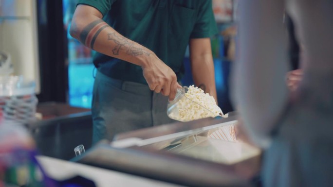 一位微笑的电影院工作人员正在为他的顾客舀爆米花。