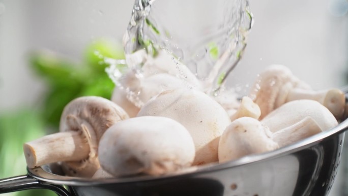 在明亮的厨房里，白色的香菇在流动的水下用滤器冲洗，慢动作