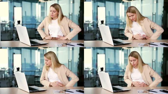 患有胃痛的年轻女商人坐在现代办公室的工作场所用笔记本电脑工作