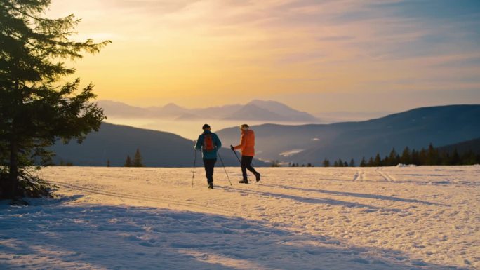 黄昏时分，一对老年夫妇带着他们的伯尔尼山狗在雪山上徒步旅行