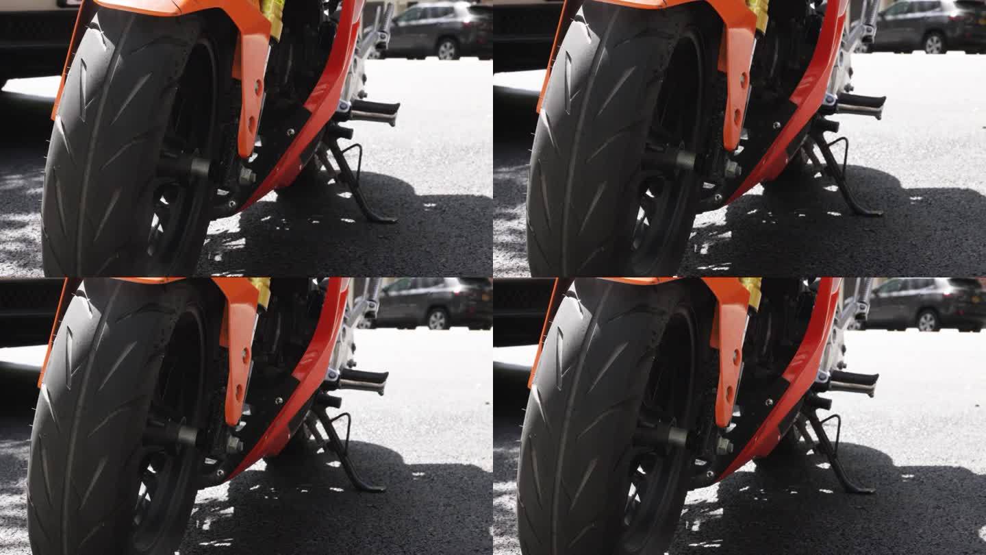 亮橙色的摩托车横坐在它的脚架上，黑色的街道胎面轮胎，在黑色的沥青上投下阴影